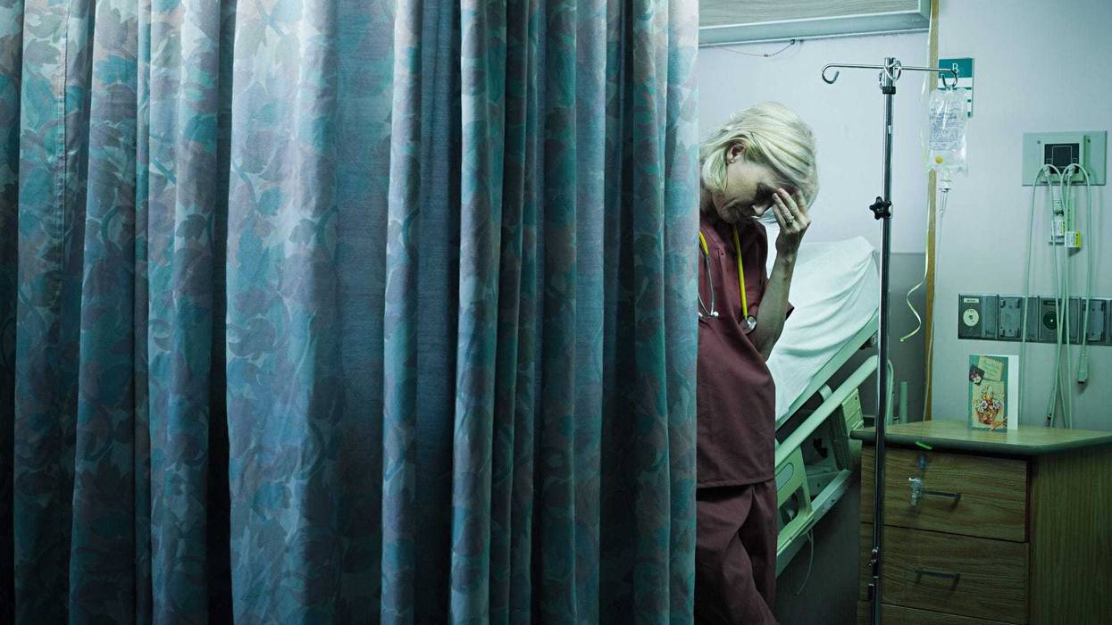 Sad nurse in hospital partially behind curtain.