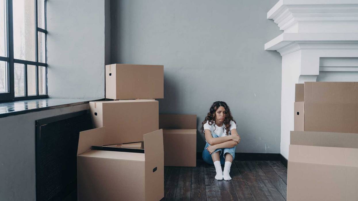 Sad woman sitting amidst packed boxes in empty room, feeling despair. Overwhelmed by divorce or eviction.