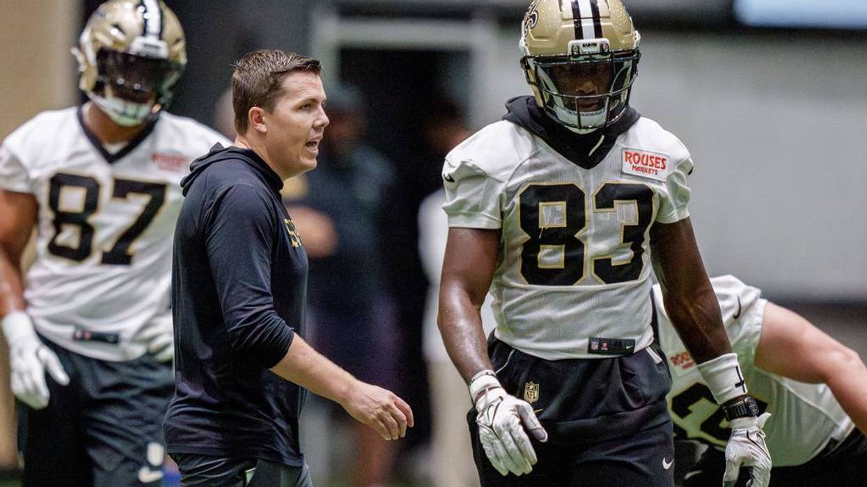 Saints coach talks to player #83 in gold helmet during indoor football practice.