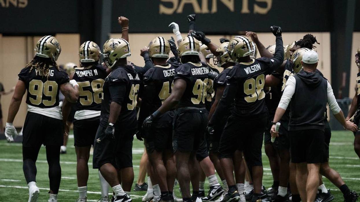 Saints football players in black and gold uniforms huddle and raise fists on the field.