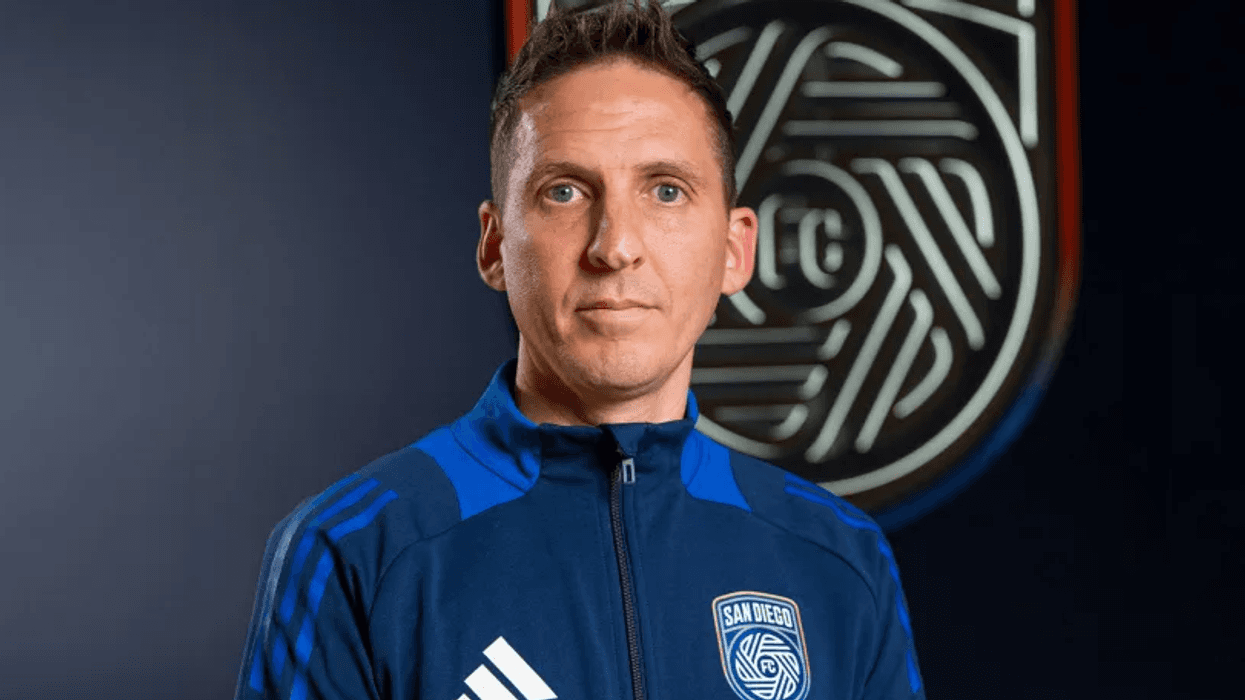 San Diego FC head coach Mikey Varas poses for a photo in front of the chrome and azul SDFC logo