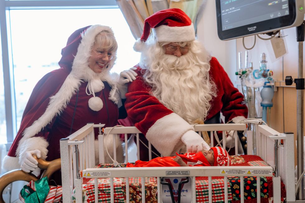 Santa, Mrs. Claus stroking tiny baby in crib