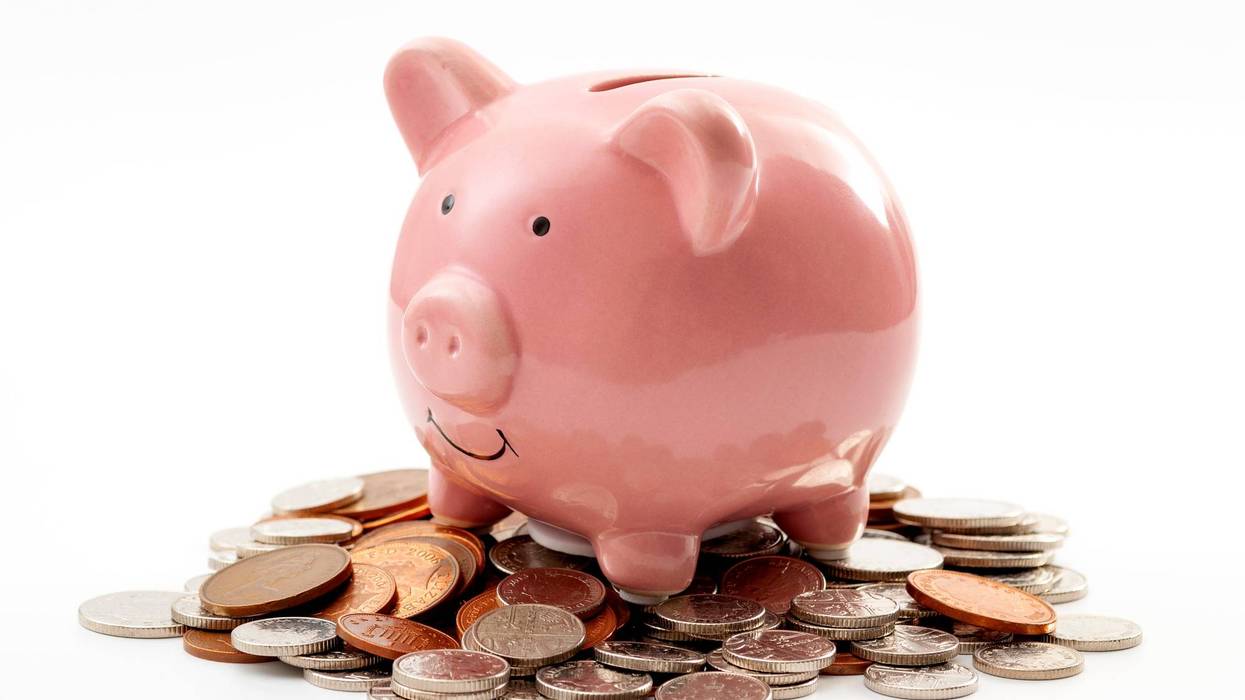 Save money, financial planning of personal finances and being thrifty concept theme with a pink piggy bank sitting on a pile of bronze and silver colored coins isolated on white background
