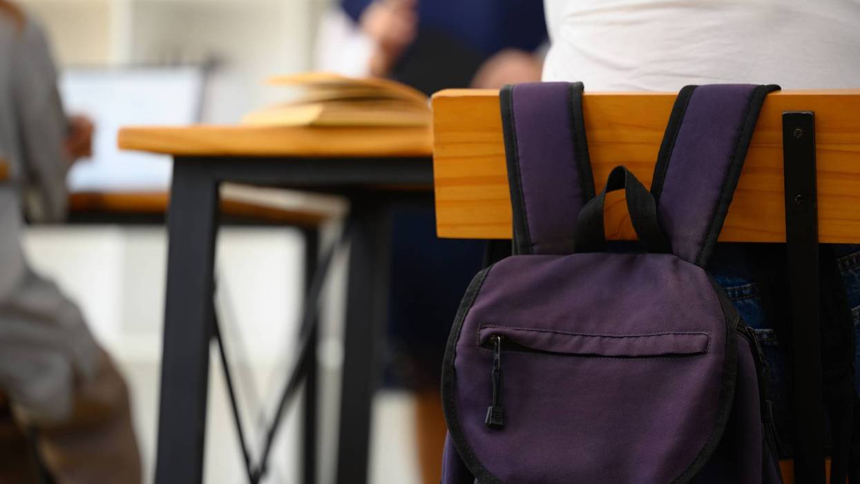 School backpack hanging on a wooden chair in classroom. Back to school concept