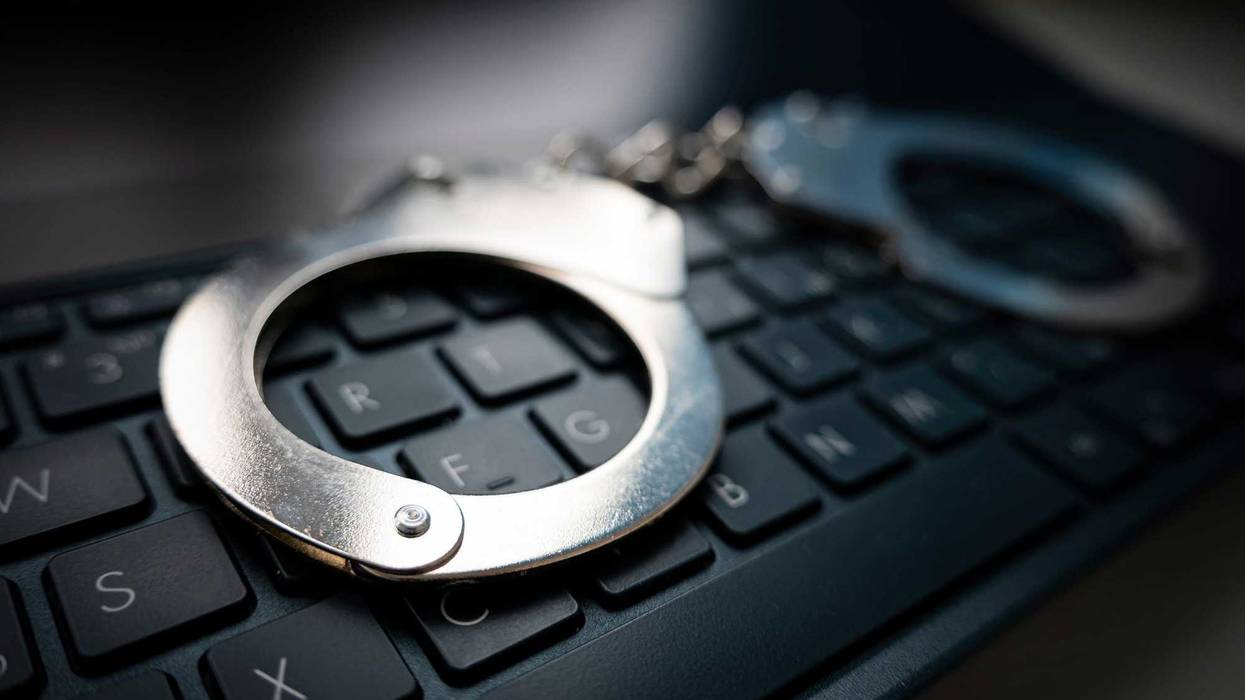 Selective focus on handcuffs on a keyboard cyber crime, hacking, bullying Against law concept in dark low key tone. metal handcuffs on a black keyboard.