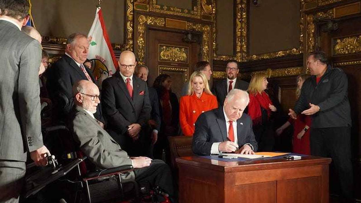 Sen Tomassoni who has ALS, watches from his wheelchair as Gov. Walz sign bill into law