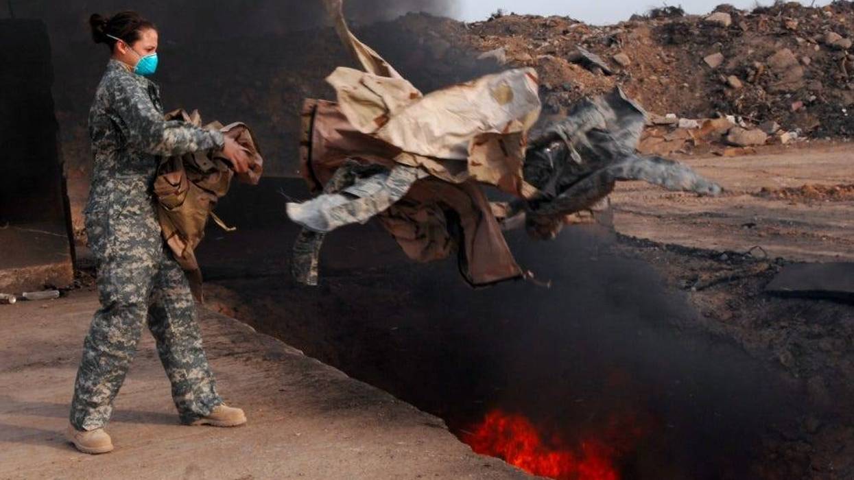 Senior Airman Frances Gavalis, 332nd Expeditionary Logistics Readiness Squadron equipment manager, tosses unserviceable uniform items into a burn pit, March 10.