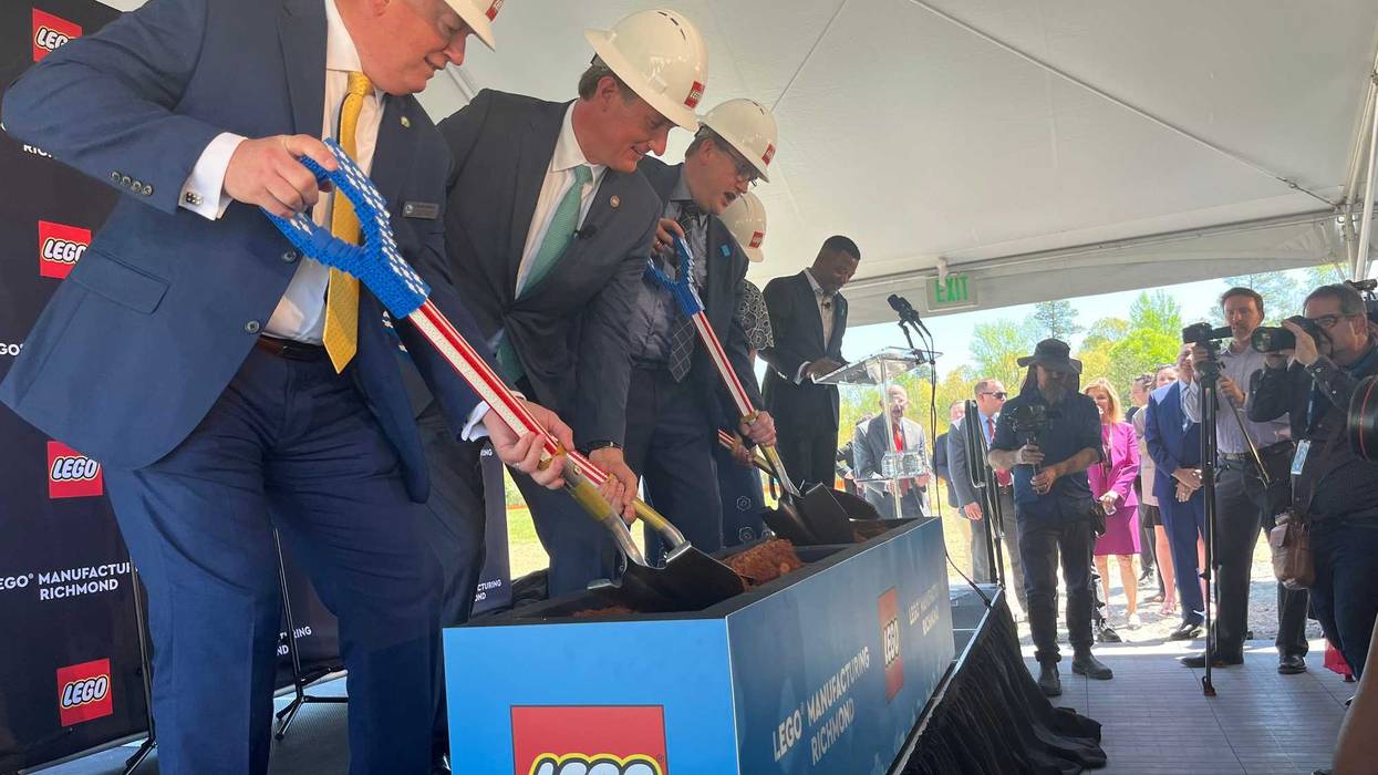 Several people stand in a line, wearing hard hats, digging
