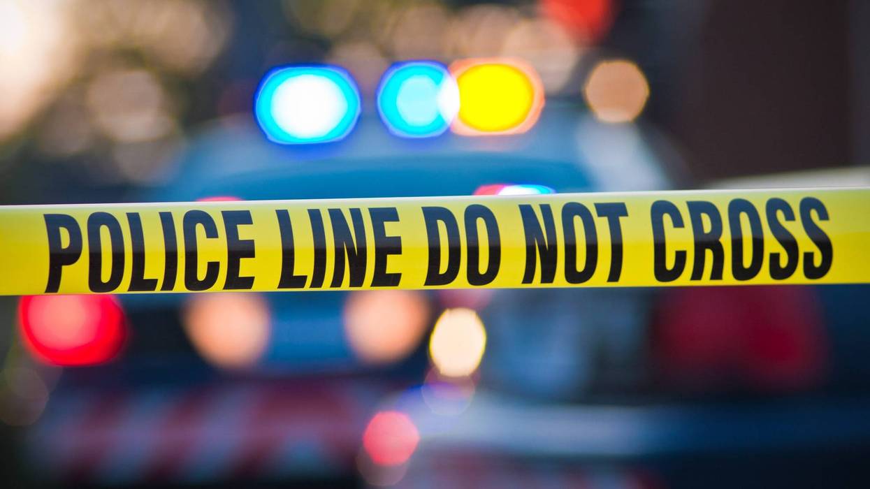 Shallow depth of field image taken of yellow law enforcement line with police car and lights in the background.