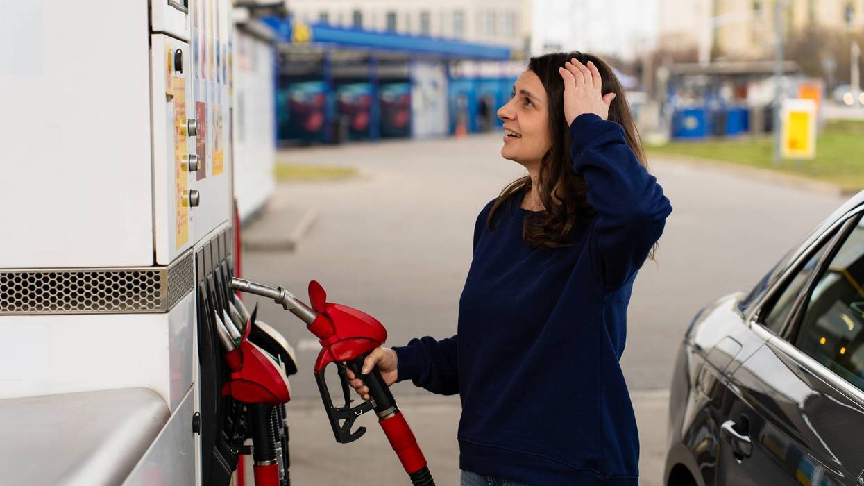 Shocked driver reacting to fuel price on pump while filling car. Woman looking surprised at fuel pump display while refueling car at gas station.