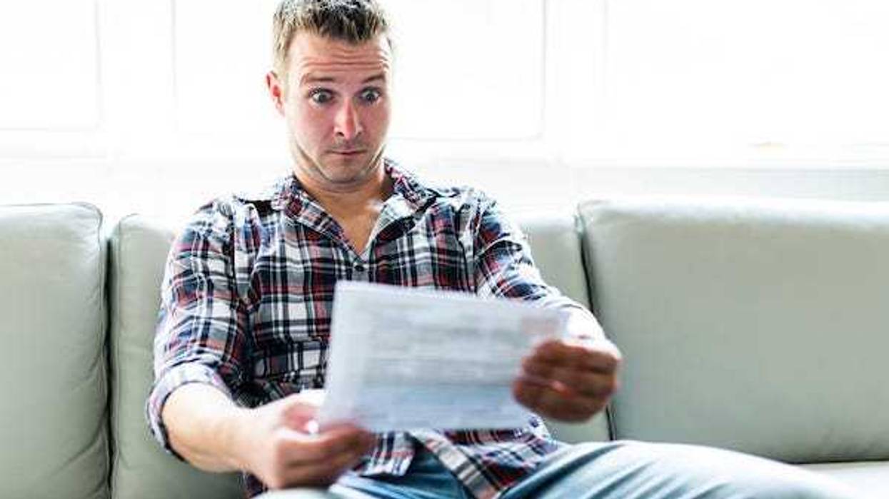 Shocked man holding documents sitting on couch