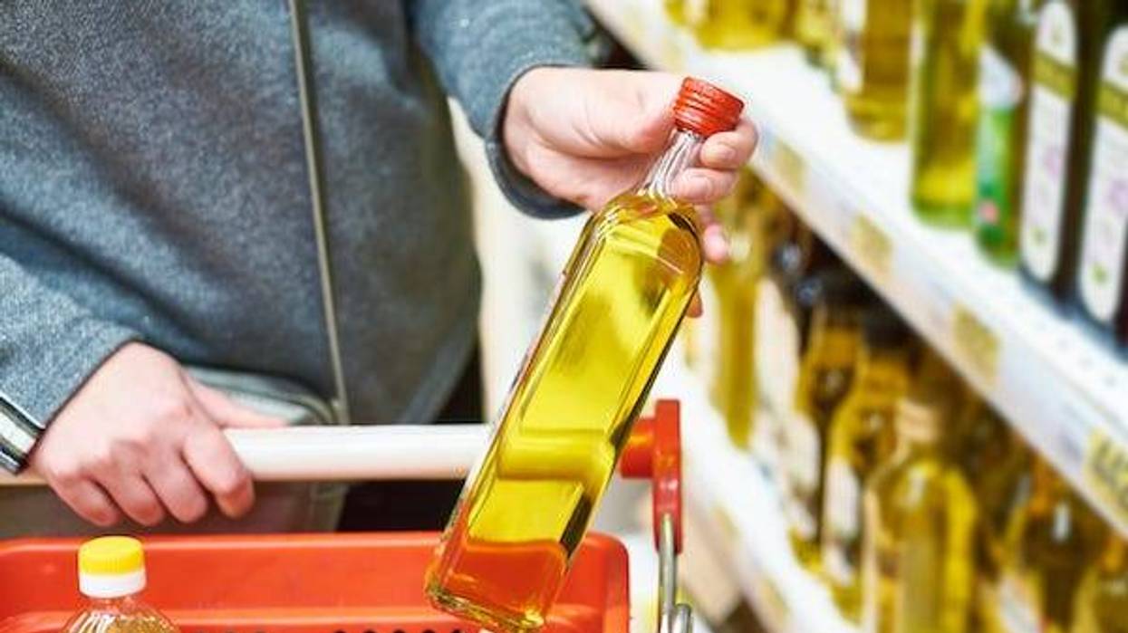 Shopper putting a bottle of olive oil in grocery cart