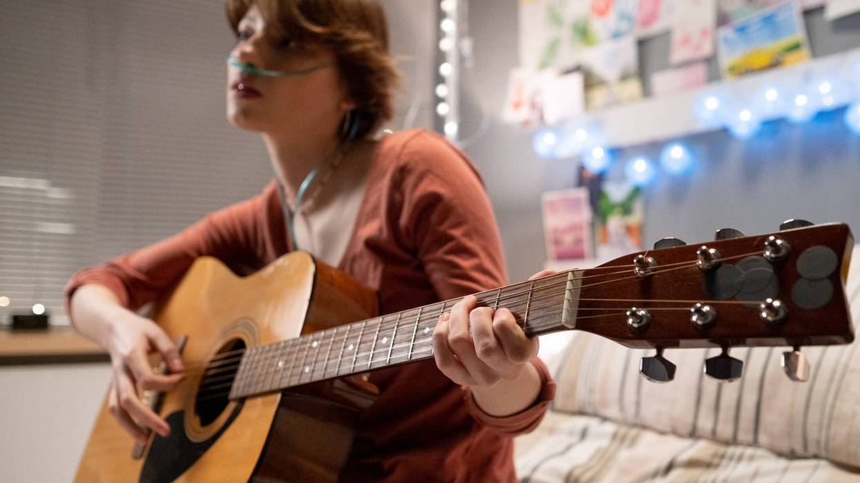 Sick girl sitting at hospital bed and playing guitar at the ward during her treatment at pandemic at hospital