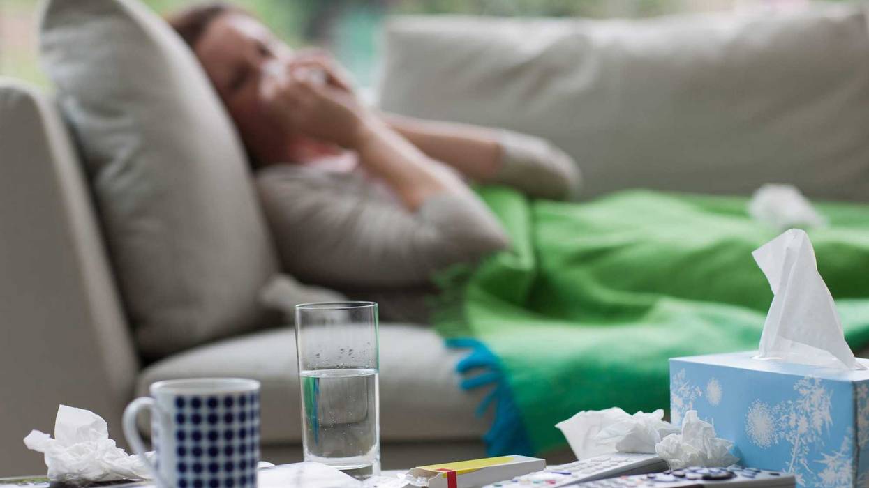 Sick woman laying on the couch with tissues, water, and other items to help her fight the sickness.
