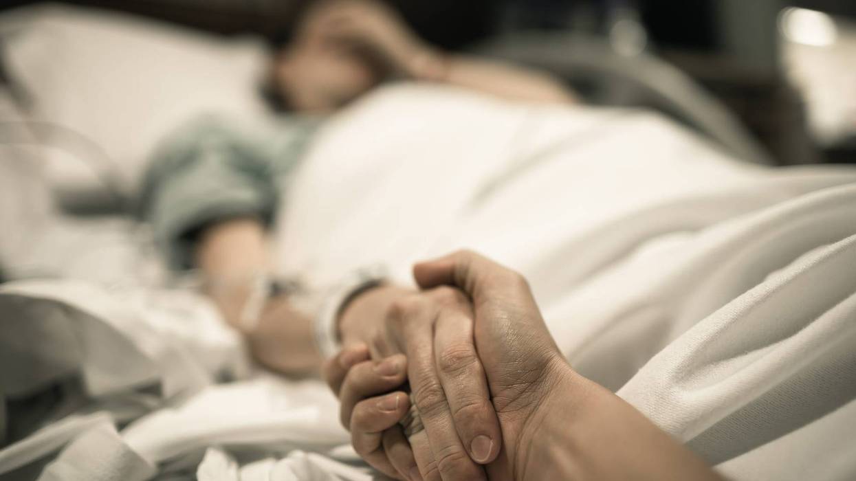 Sick woman lying in hospital bed with hand being held by love one