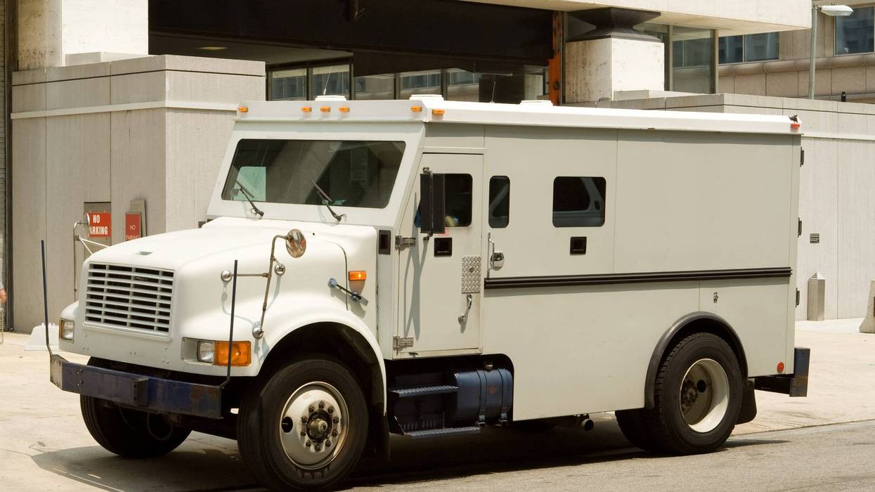 Side view of gray armored truck parked on street making a cash pickup.