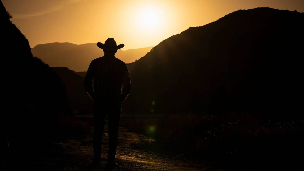 Silhouette of adult man in cowboy hat against mountain and sky during sunset