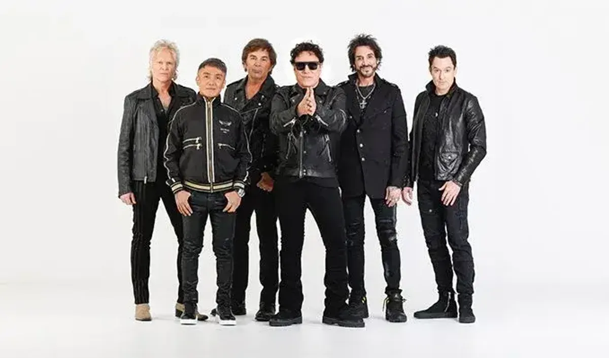 Six men, the rock band Journey, pose in black leather jackets against a white background.