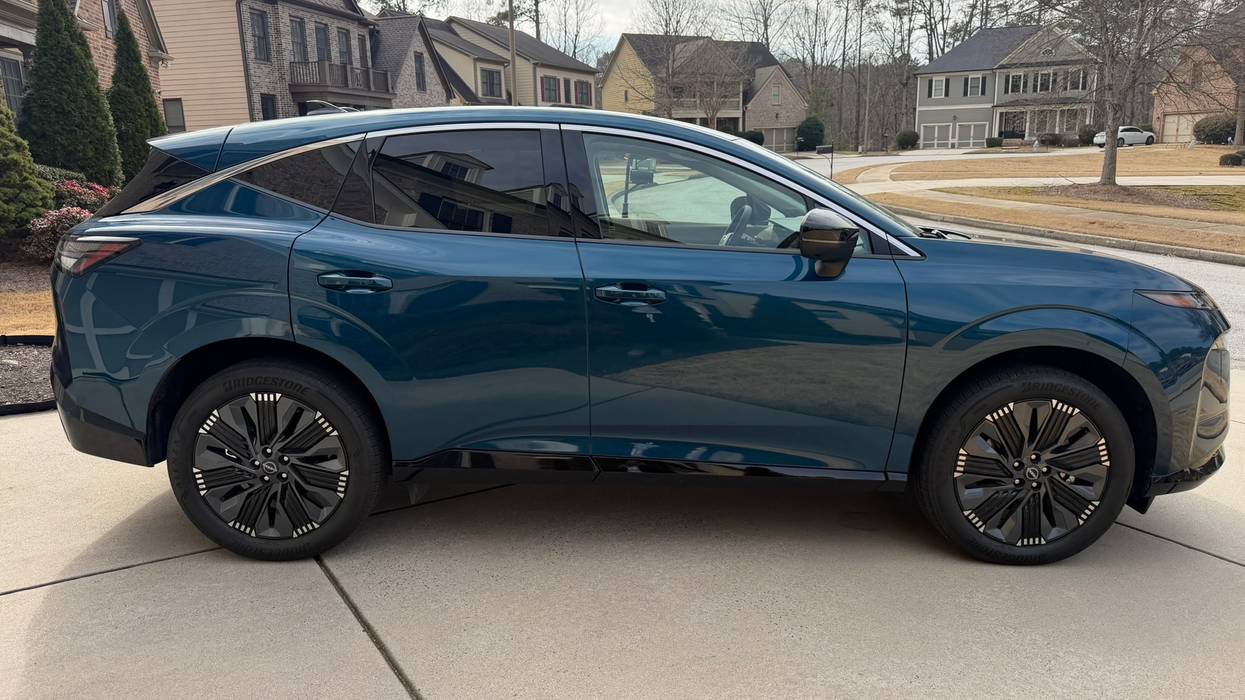 Sleek, dark teal SUV with black and white accent wheels parked on a suburban driveway.