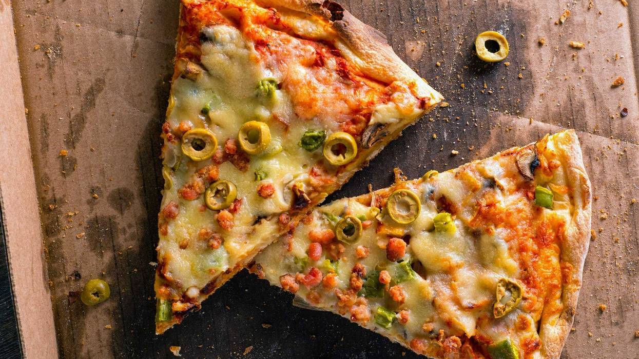 Slices of cold messy leftover pizza in a delivery box.