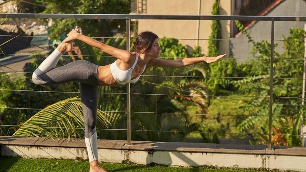 Slim young lady is practicing asana on terrace in open air. She is balancing on one foot and stretching body