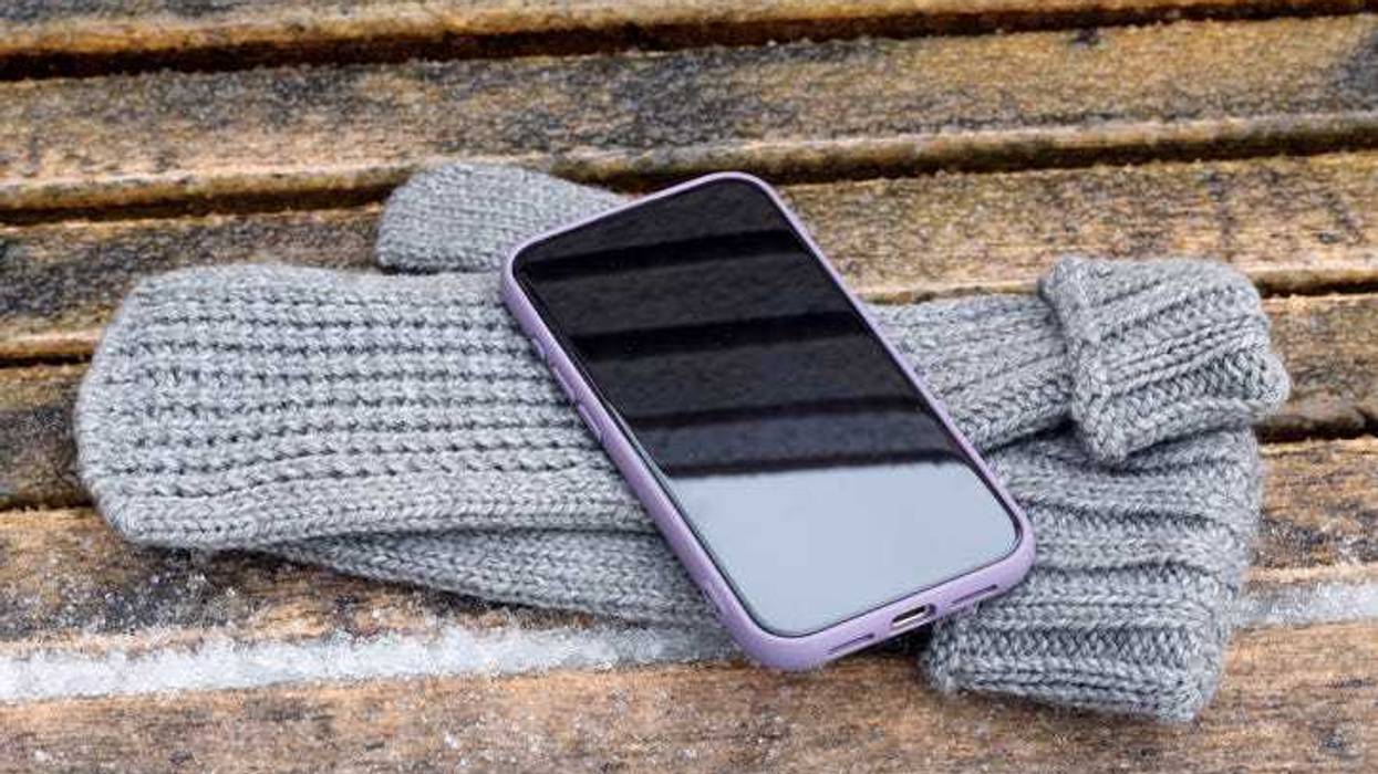 Smartphone with purple case resting on grey knitted mittens during winter in outdoor setting