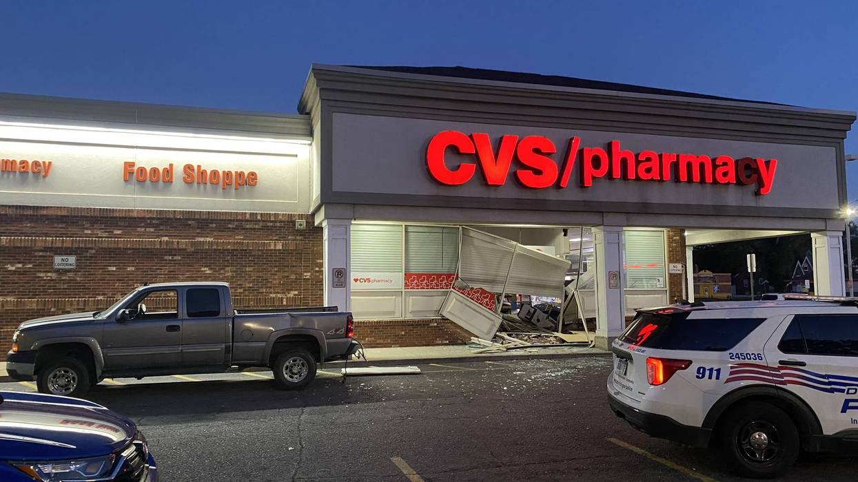 Smashed CVS Pharmacy entrance with a police SUV and a pickup truck nearby at dusk.
