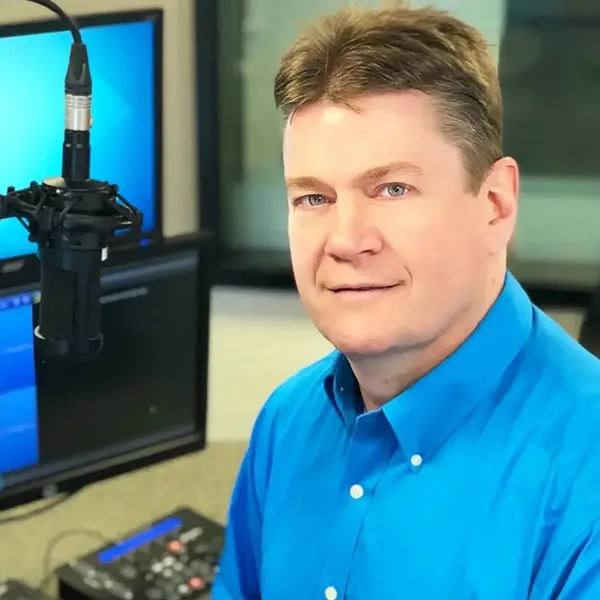Smiling man in blue shirt with microphone in a studio setting.