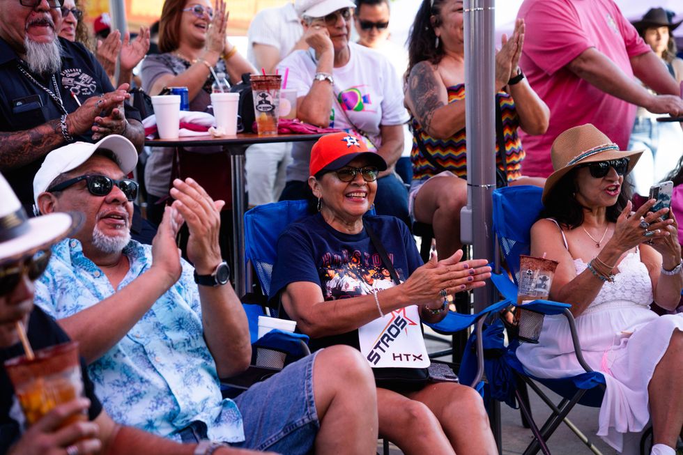 Smiling people, including Houston Astros fans, clapping at an outdoor event.