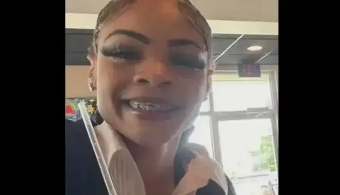Smiling person with braces and prominent eyelashes, holding a straw. Indoor setting.