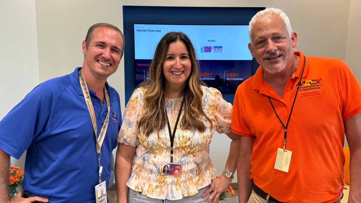 Smiling woman between two men in an office. One man wears an orange MDOT shirt.