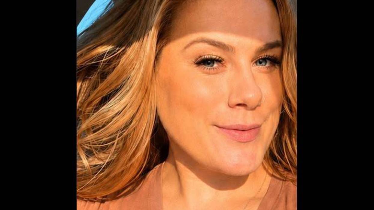 Smiling woman with blonde hair and blue eyes, bathed in sunlight with a brow shadow.