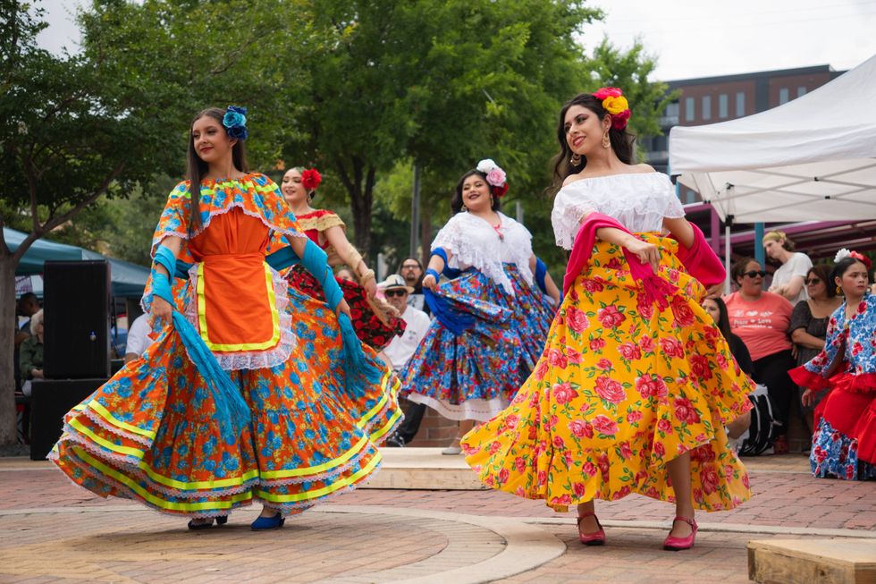 Smiling women in vibrant Mexican folk dresses dancing outdoors.