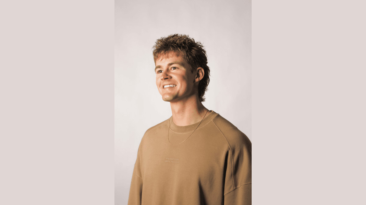 Smiling young man with textured hair in a brown sweatshirt, looking right.