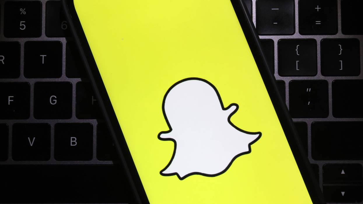 Snapchat logo on yellow phone screen, with computer keyboard in background
