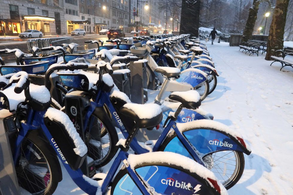 Snow piles up on Citi Bikes as a person walks along Central Park South on January 16, 2024