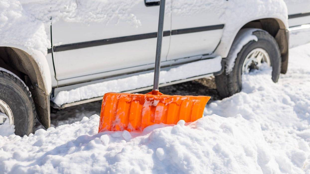 Snow shovel sticking out from snowdrift in front of snow covered SUV - stock photo