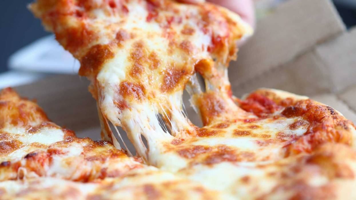 Someone pulling a piece of pizza onto their plate.