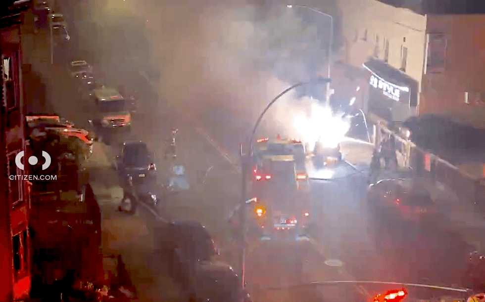 Sparks and flames erupt from a burning vehicle as firefighters respond to the scene