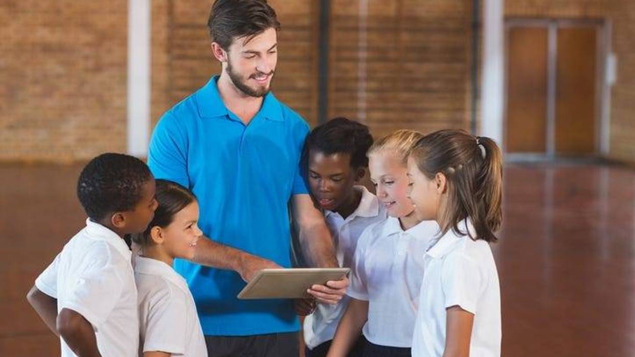 Sports teacher and school kids using digital tablet in basketball court at school gym