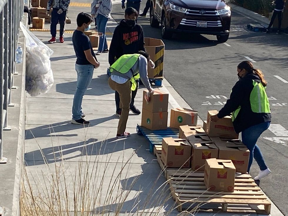 Staff stack boxes at the "Feeding 5,000" food giveaway event at the Cow Palace.
