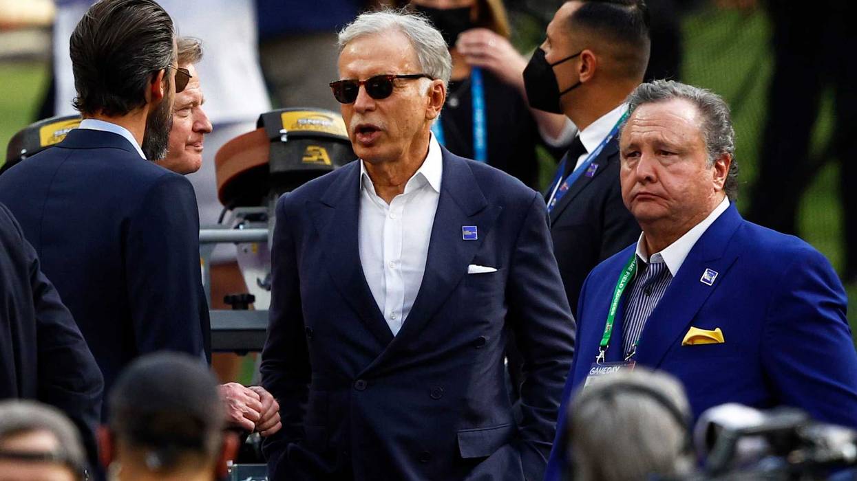 stan kroenke wears sunglasses and a suit surrounded by people at a football game