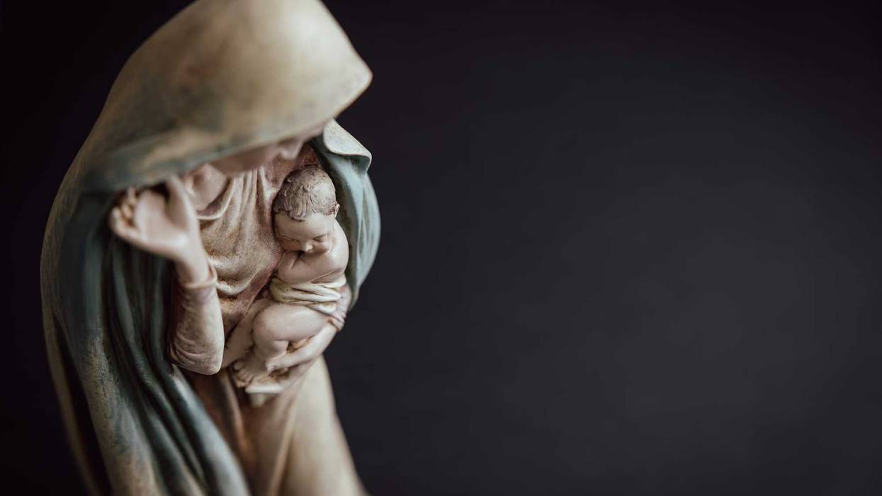 Statue of the virgin Mary holding the baby Jesus against a black background with copy space