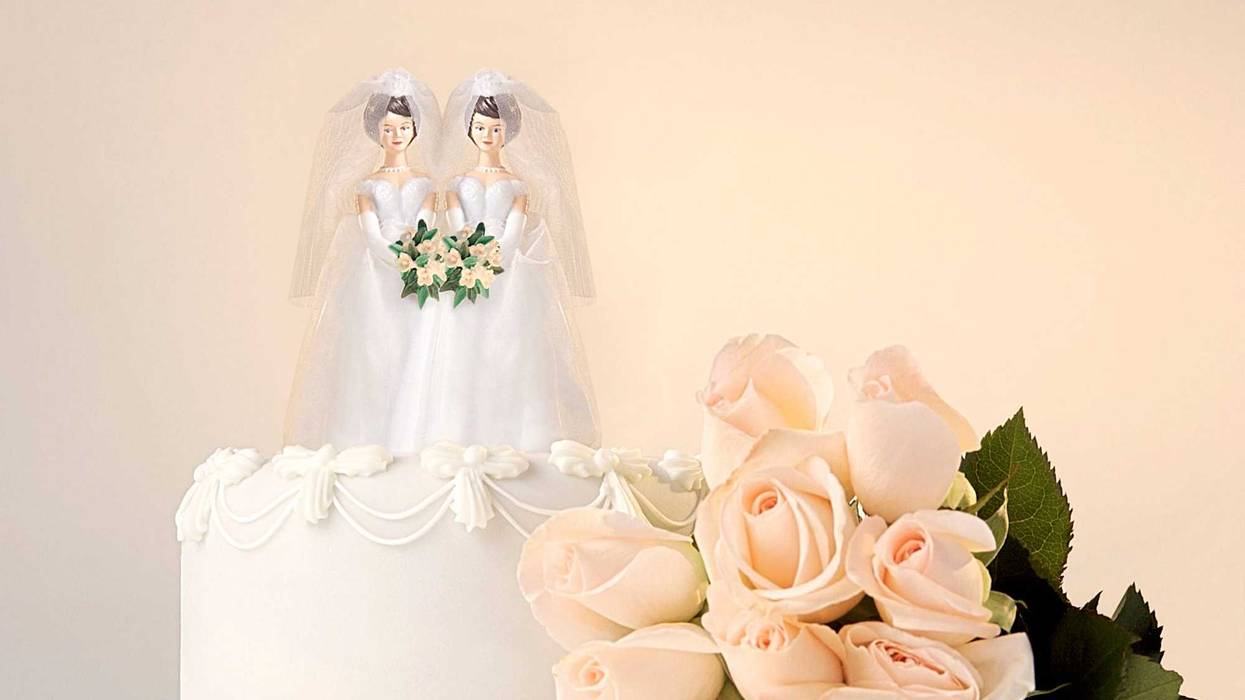 Still life of the top of a wedding cake with two miniature brides cake topper and roses at the side