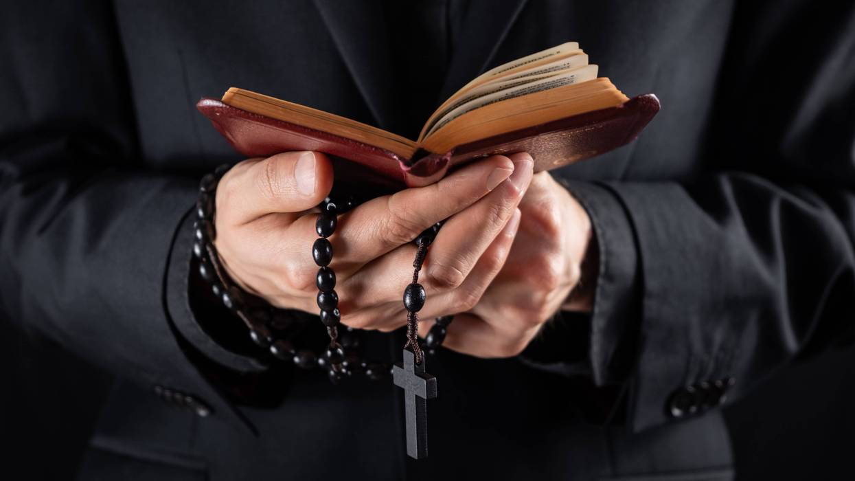 stock image of a priest holding a bible and rosary beads