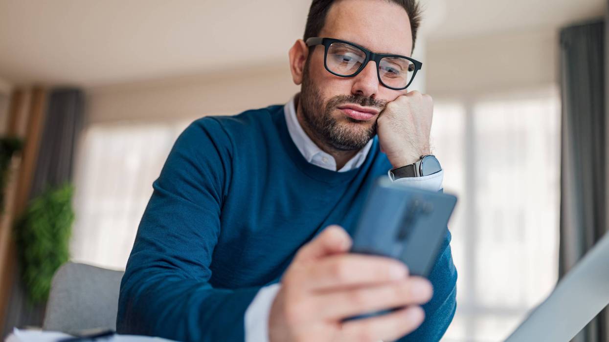 stock photo of man with laptop out in front of him scrolling on his phone