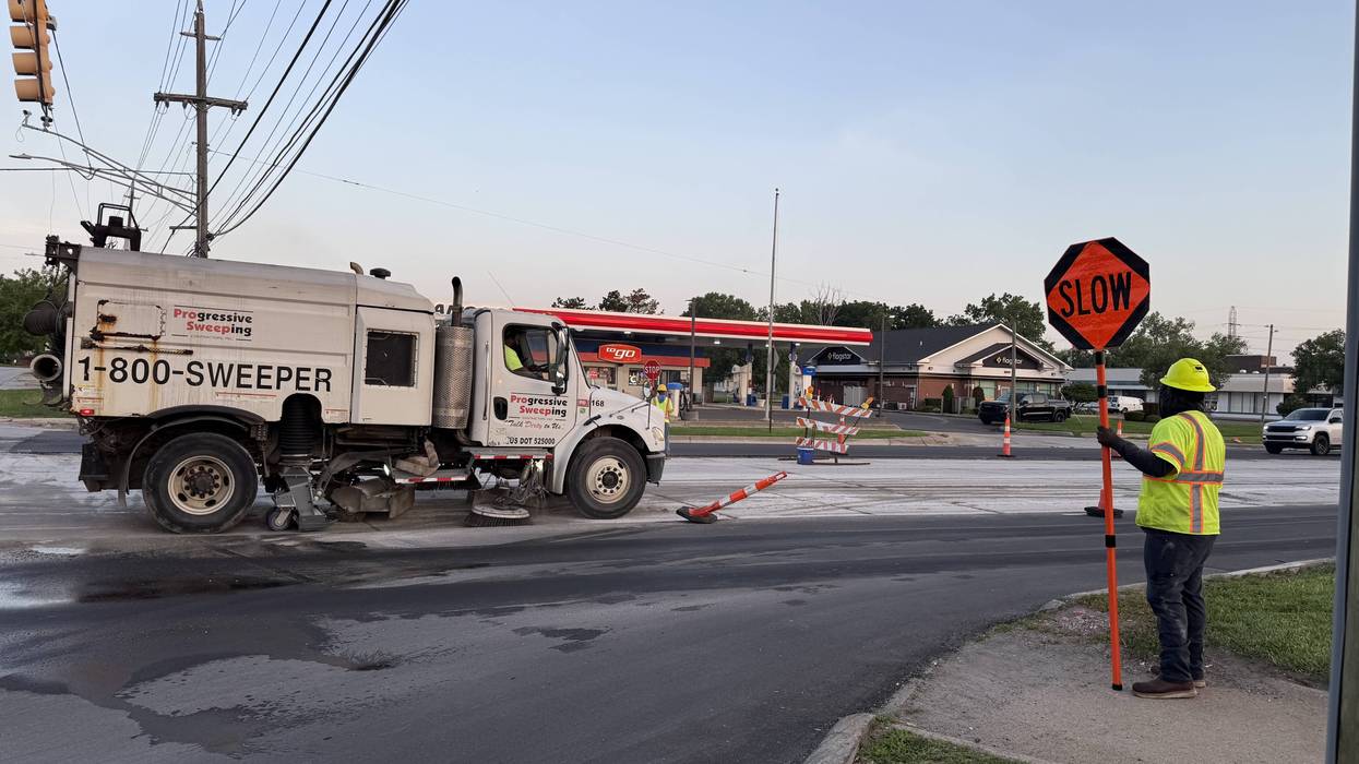 Street sweeper truck and a flagger holding a "SLOW" sign during road work.