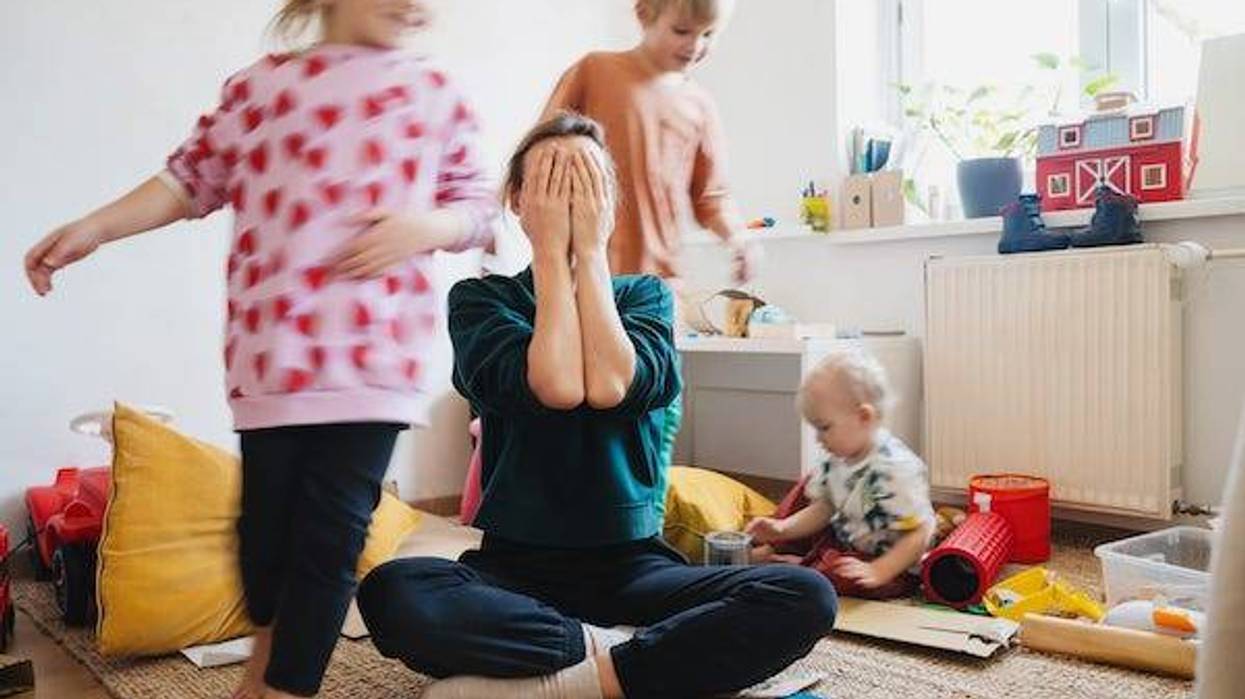 Stressed mom sitting on floor with children running around her