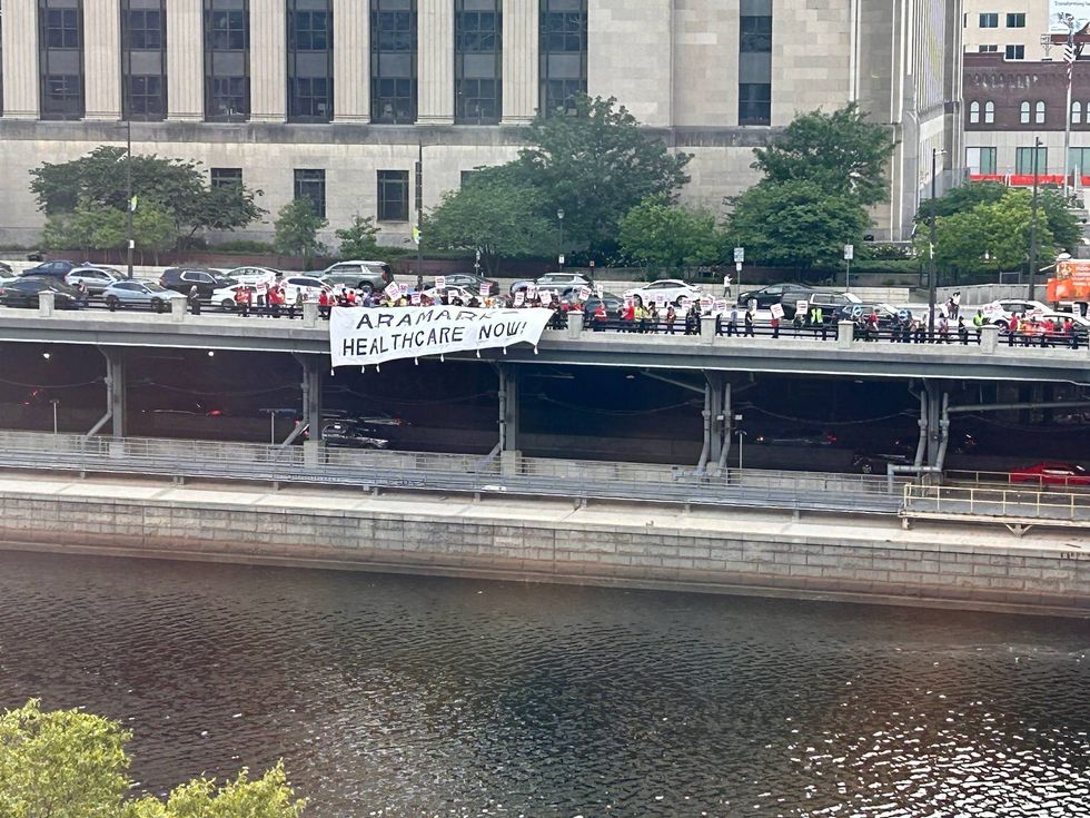 Striking workers unfurled a banner reading "Aramark health care now" and hung it over the Schuylkill Avenue guardrail, across the river from Aramark