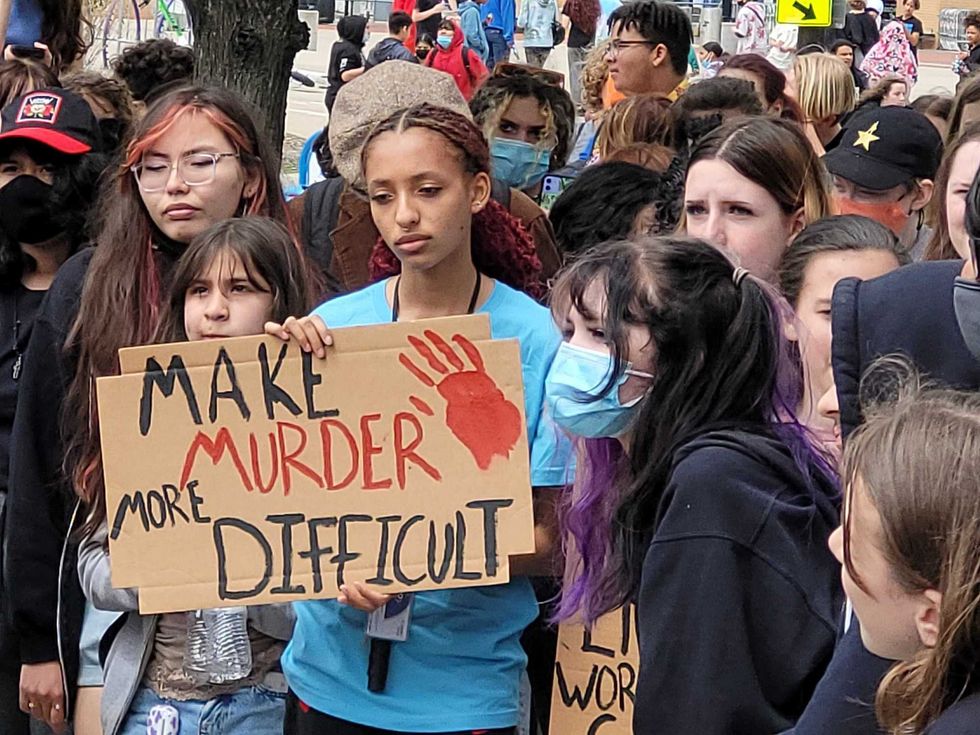 student at gun control rally with sign says, "make murder difficult"